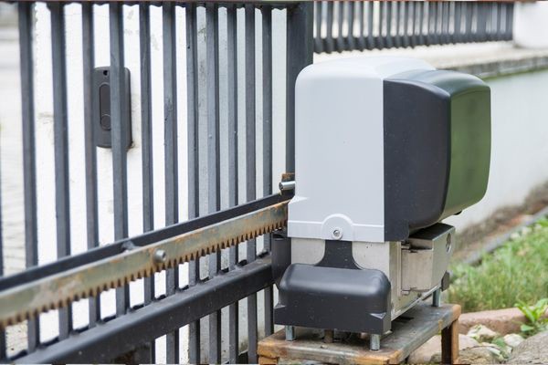 An automatic sliding gate opener installed next to a metal gate in Austin. The motor is encased in a gray and black housing and mounted on a sturdy platform. A toothed metal track runs along the bottom of the gate, engaging with the opener mechanism, making repairs straightforward and efficient.